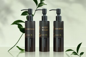 Drie zwarte flessen met de aanduidingen 'BODY CONDITIONER', 'BODY WASH' en 'SHAMPOO', met gouden tekst en een groene bladsymbool.