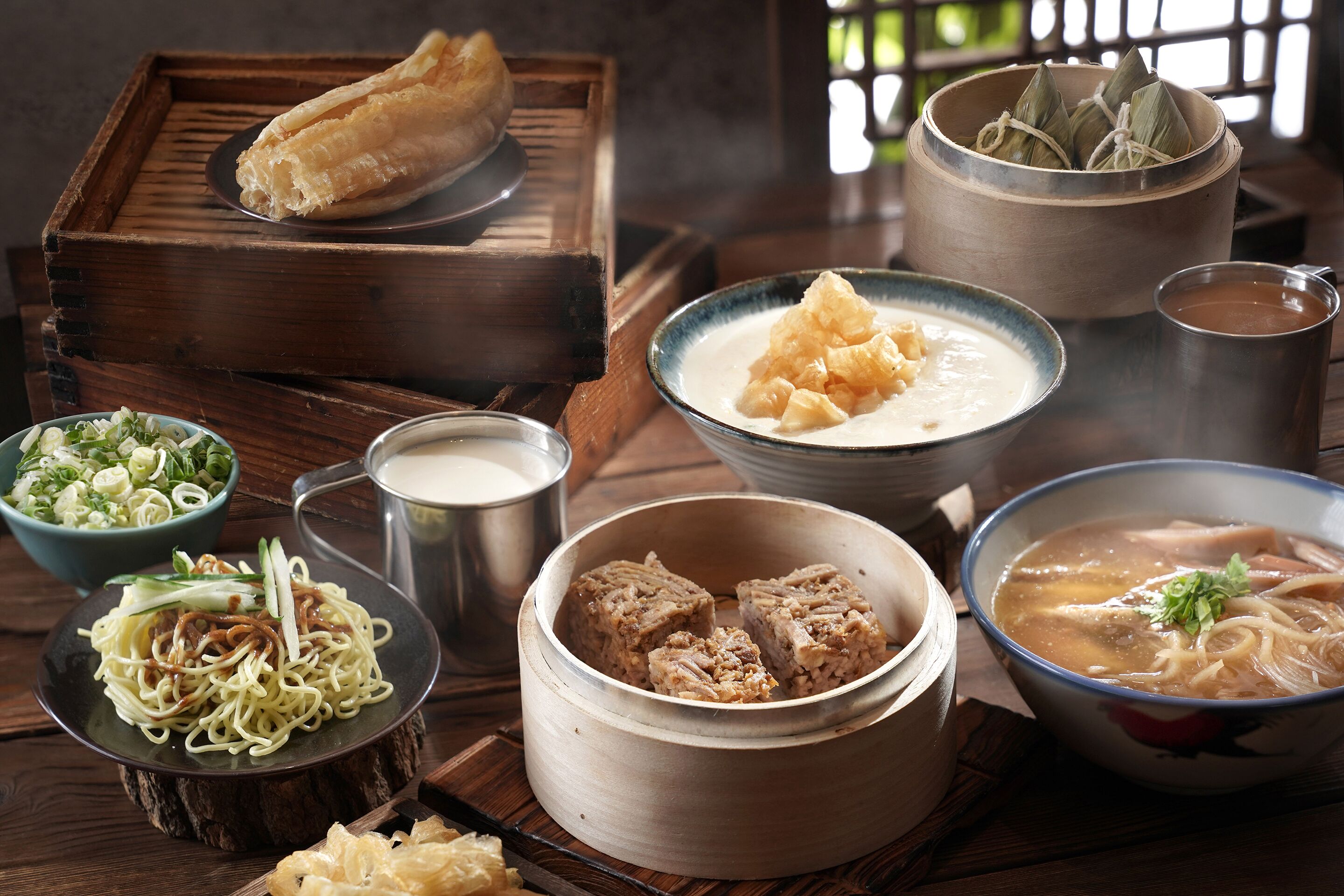 On y trouve une variété de plats traditionnels, notamment un bol de soupe, une assiette de nouilles et plusieurs autres plats présentés sur un plateau en bois.