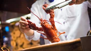 A chef holding a lobster with tongs, in a kitchen setting.