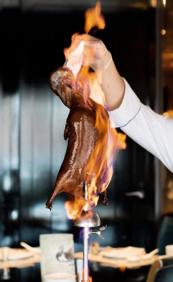 A person holding a roasted pig over a flame. - Palais de Chine Hotel (Taipei)