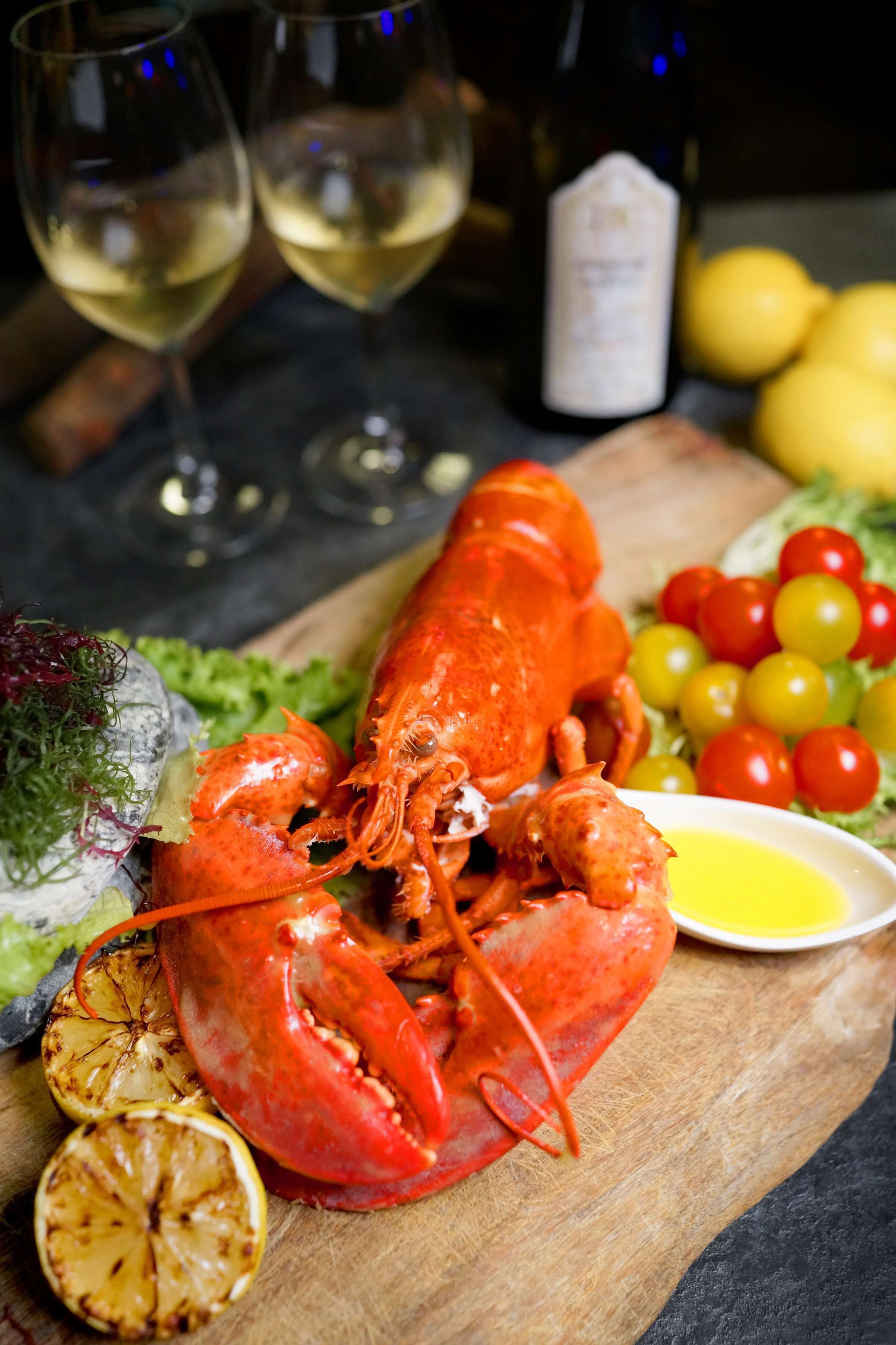A lobster on a wooden board with lemon slices, cherry tomatoes, and a bottle of wine.