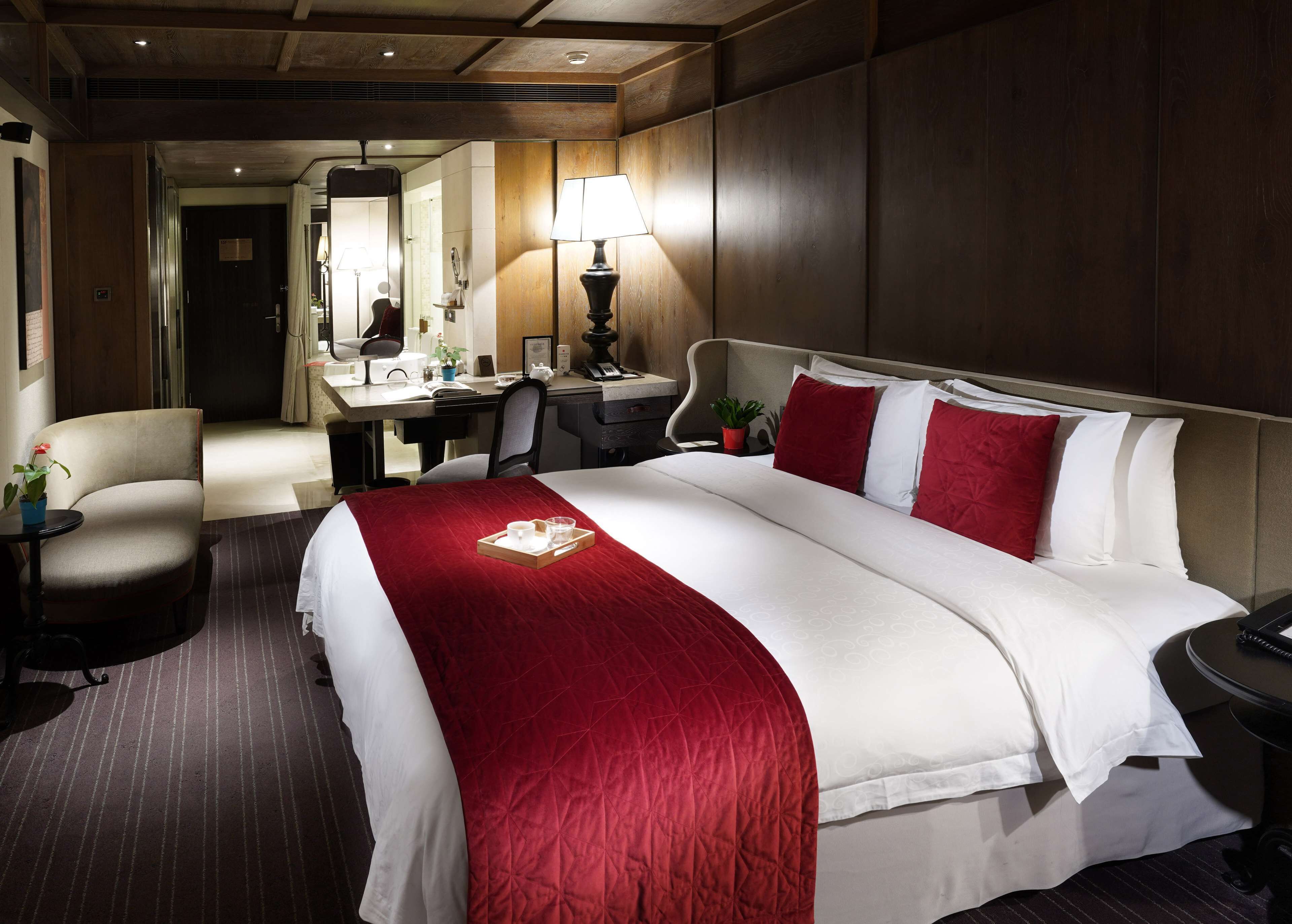 A hotel room with a large bed, a desk, a chair, a lamp, and a mirror.