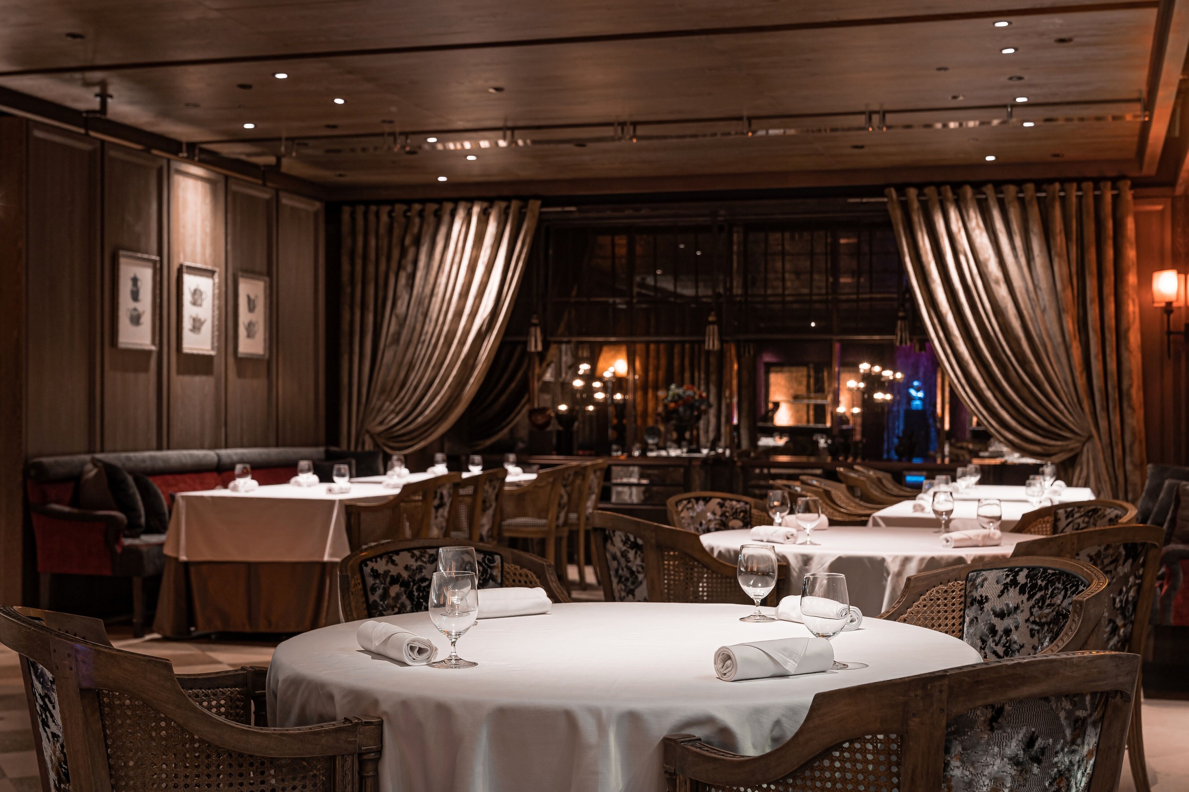 Een restaurant met ronde tafels, houten stoelen en gordijnen.