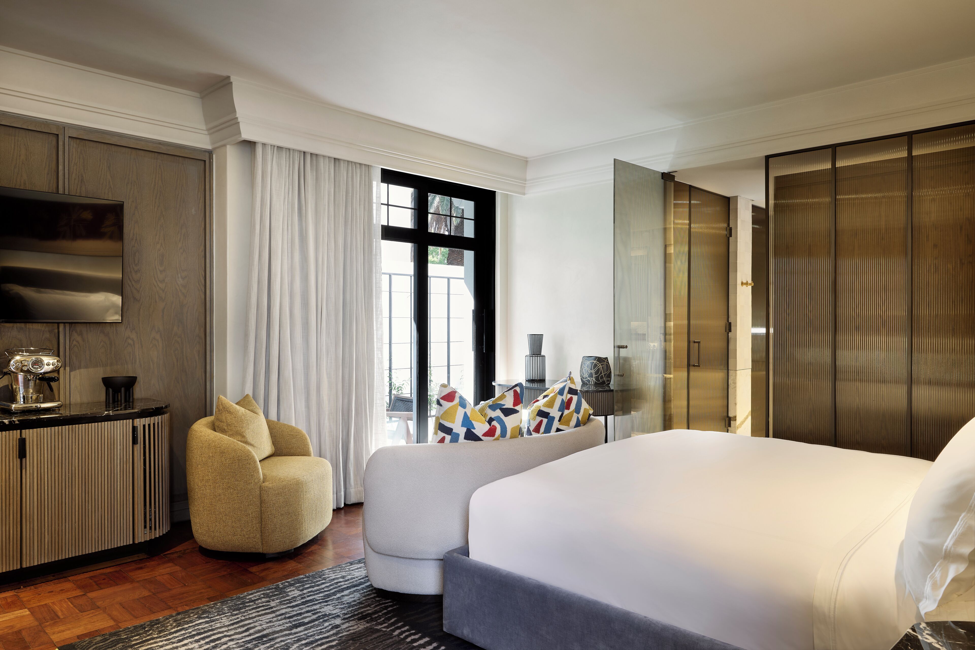 Quarto de hotel moderno com uma cama grande, um sofá, uma TV e um guarda-roupa.