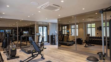 Un gimnasio con máquinas de cardio, bancos de pesas y un espejo grande.