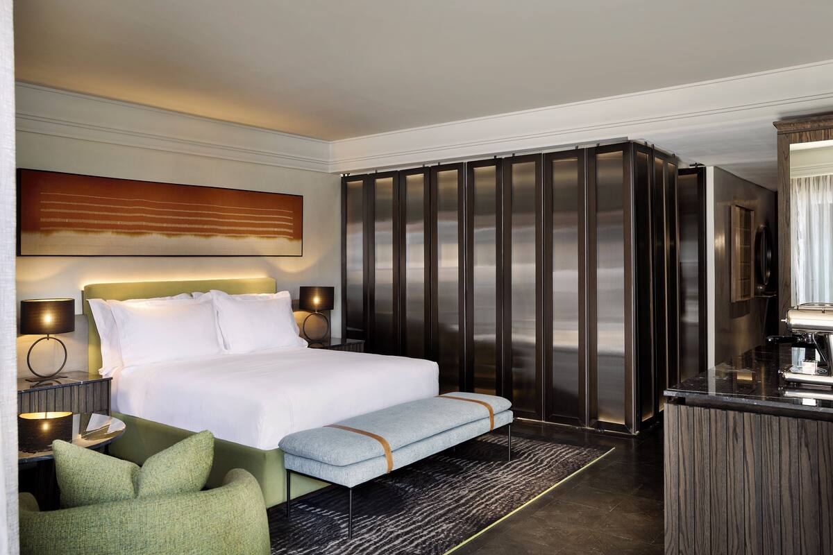 Une chambre d’hôtel avec un grand lit, un banc, un bureau et une armoire.