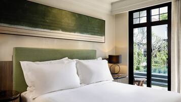 Una habitación de hotel con una cama, cabecera verde, un ventanal grande y un cuadro en la pared.
