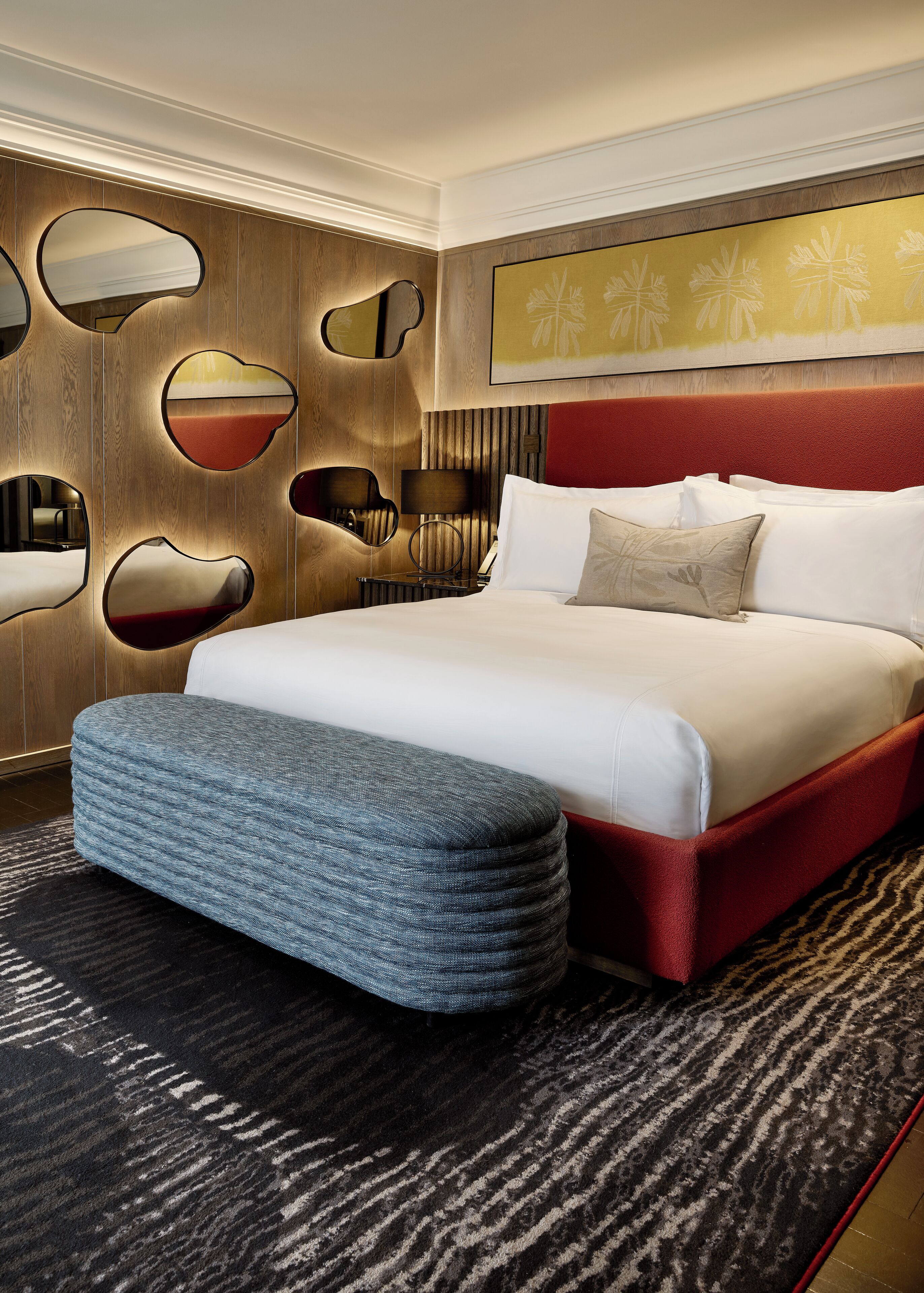 Une chambre d’hôtel moderne dotée d’un grand lit, d’une tête de lit rouge et d’un décor mural original agrémenté de miroirs.