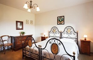A bedroom with a four-poster bed, a wooden dresser, a chair, and a nightstand with a lamp. - Tenuta delle Ripalte (Capoliveri)