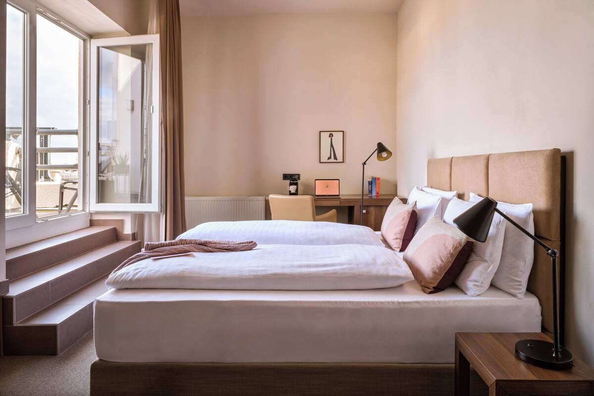 Quarto de hotel com uma cama grande, uma escrivaninha com um laptop e vista para o exterior.