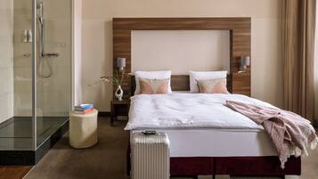 A hotel room with a bed, a bedside table, a lamp, a shower, and a suitcase.