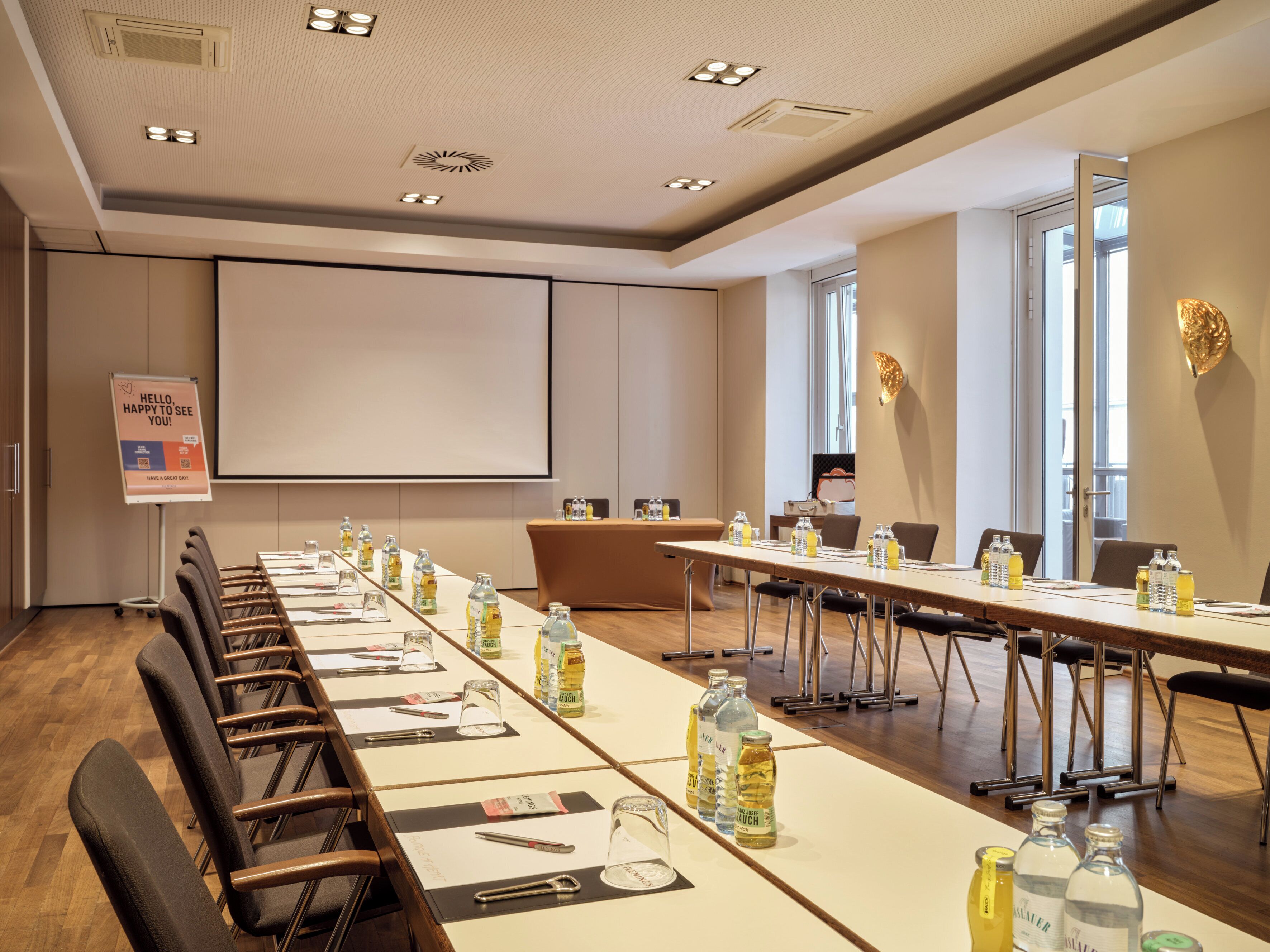 Un salón de conferencias con mesas largas, sillas y una pantalla para proyector.