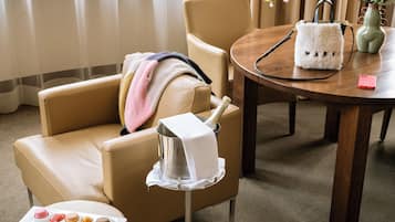 Una habitación de hotel moderna con un sofá de cuero, una mesita redonda con una botella de champán, un florero con flores y un teléfono rosa sobre la mesa.