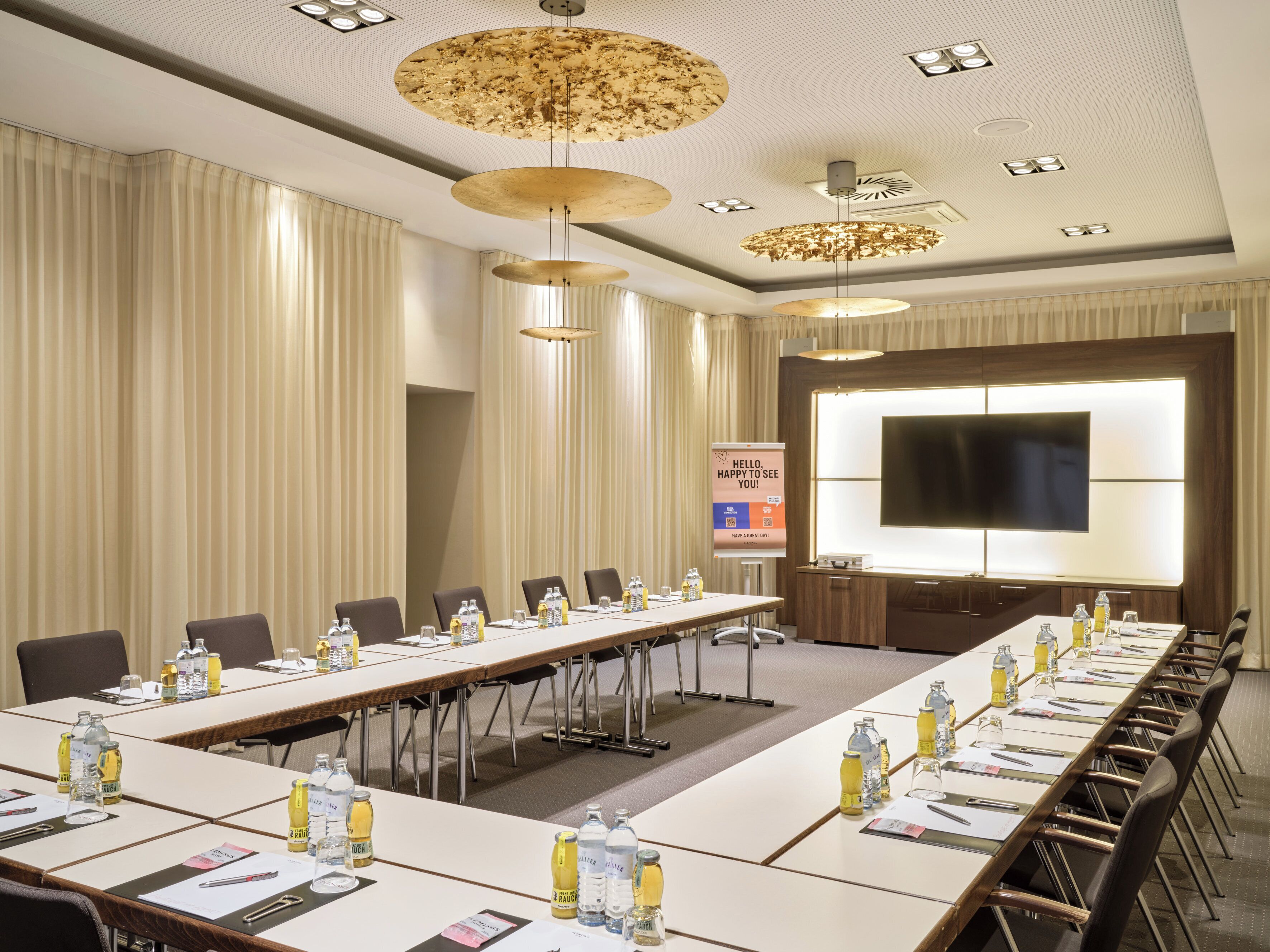 A conference room with a long table, chairs, water bottles, and a large screen.