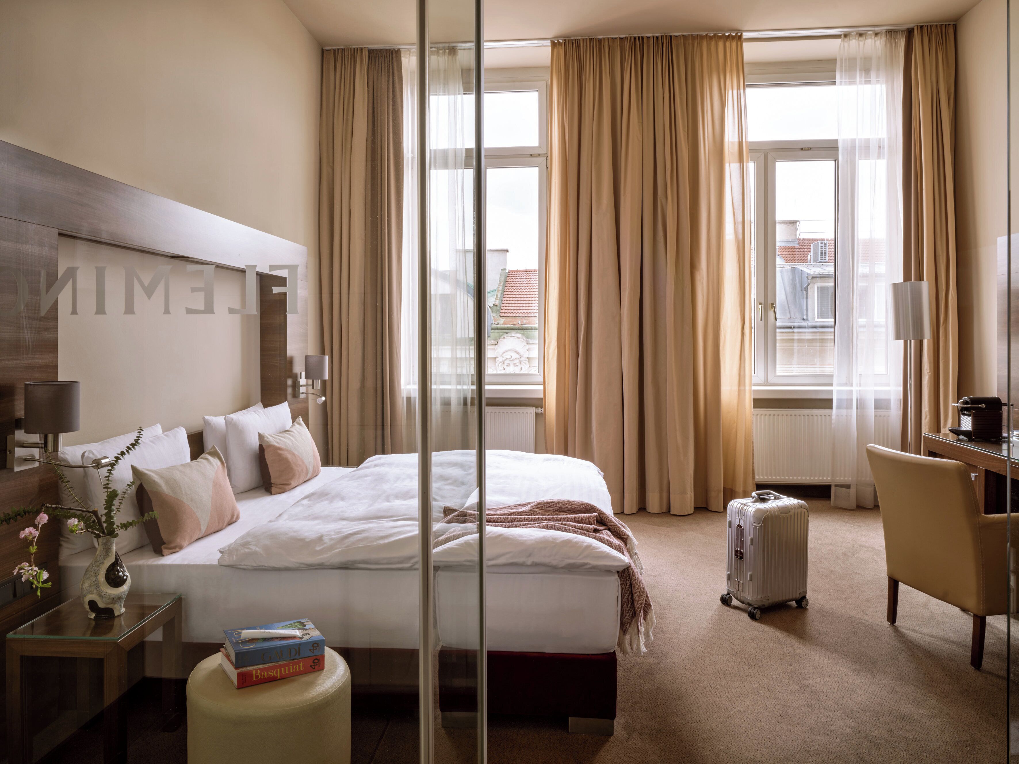 A hotel room with a large bed, a desk, a chair, a lamp, a radiator, and a window with curtains.