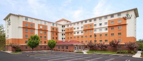 A multi-story hotel with a modern design, featuring a central entrance and a parking lot in front.