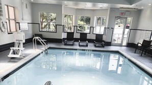 Una piscina interior con agua cristalina, rodeada de paredes con azulejos blanco y negro, y equipada con barandillas de seguridad.