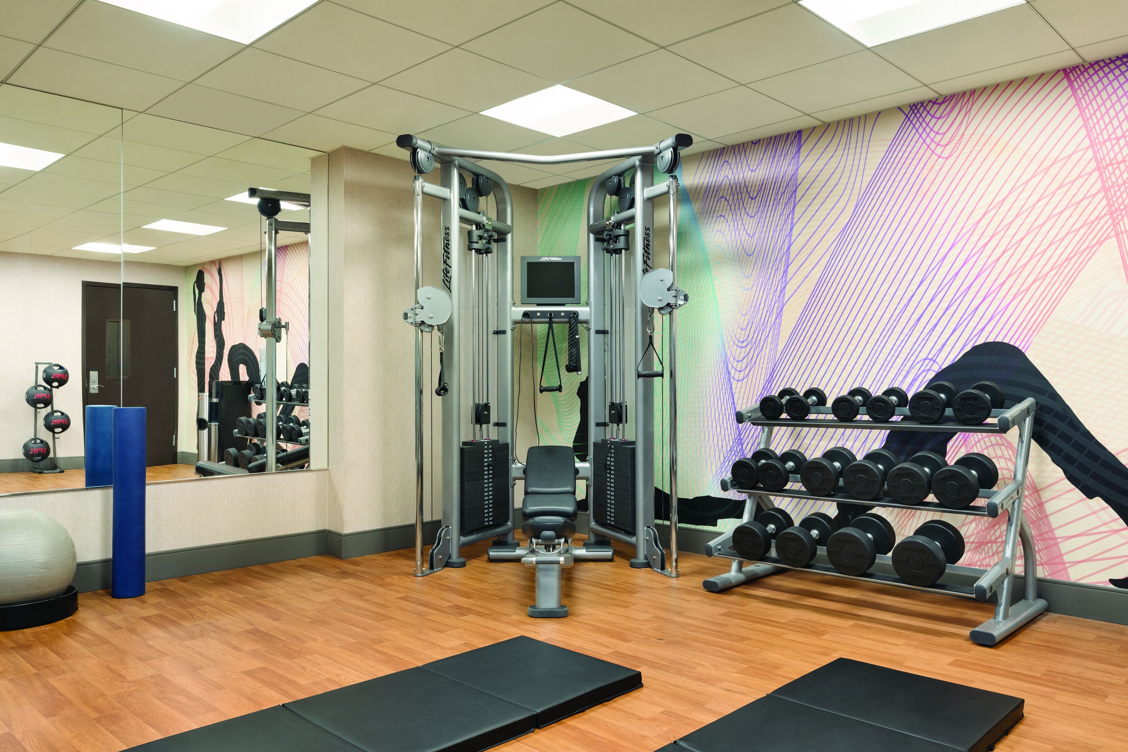 A gym with exercise equipment, a mirror, and a wall with a colorful design.