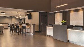 Un vestíbulo de hotel moderno con mostrador de recepción, zona de bar y asientos.