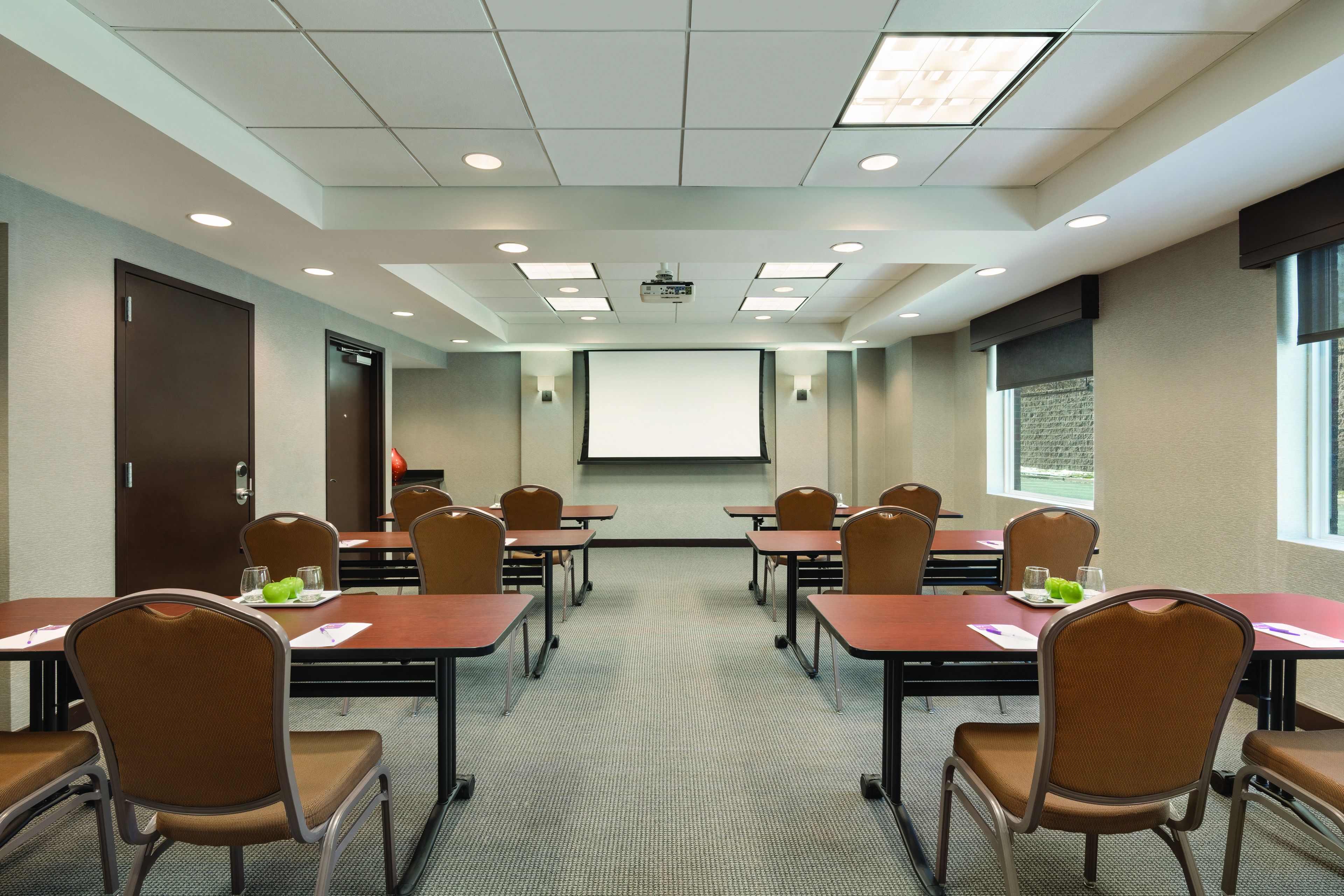 Una sala conferenze con schermo per proiettore, tavoli, sedie e pavimento rivestito di moquette.