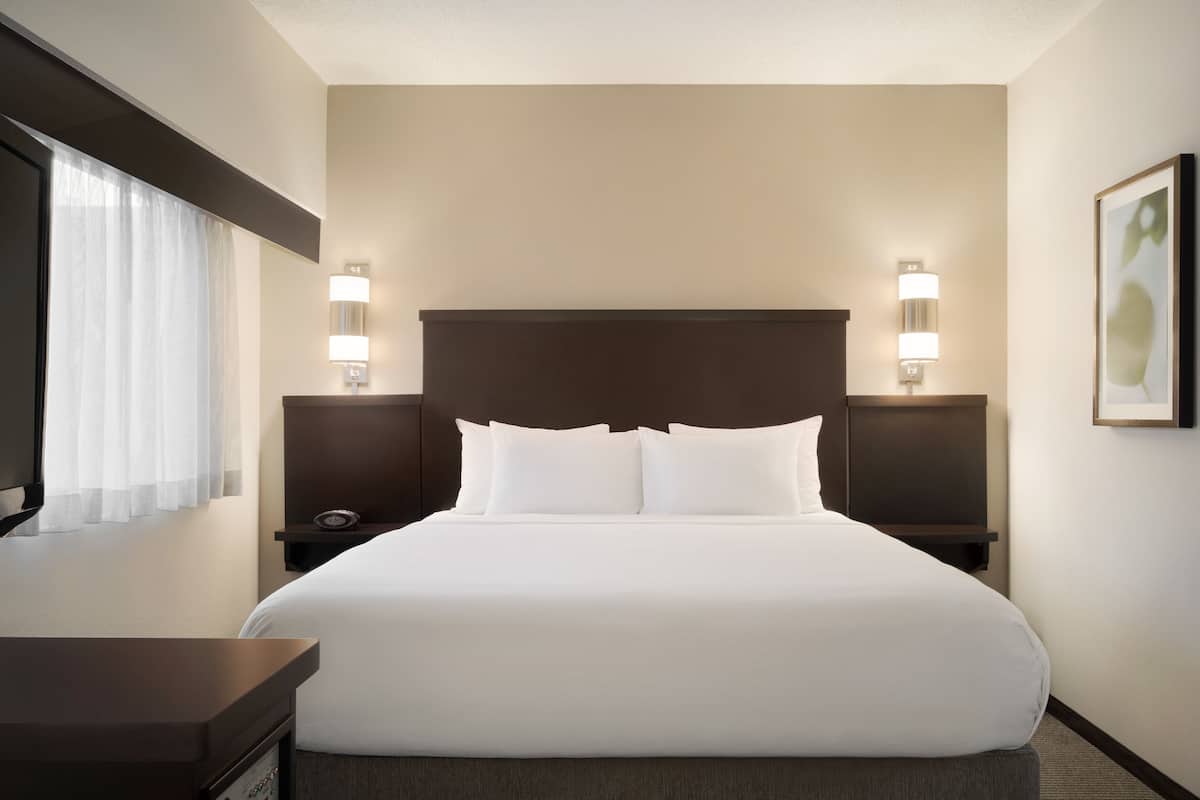 A hotel room with a large bed, two bedside tables with lamps, a nightstand, and a framed picture on the wall.