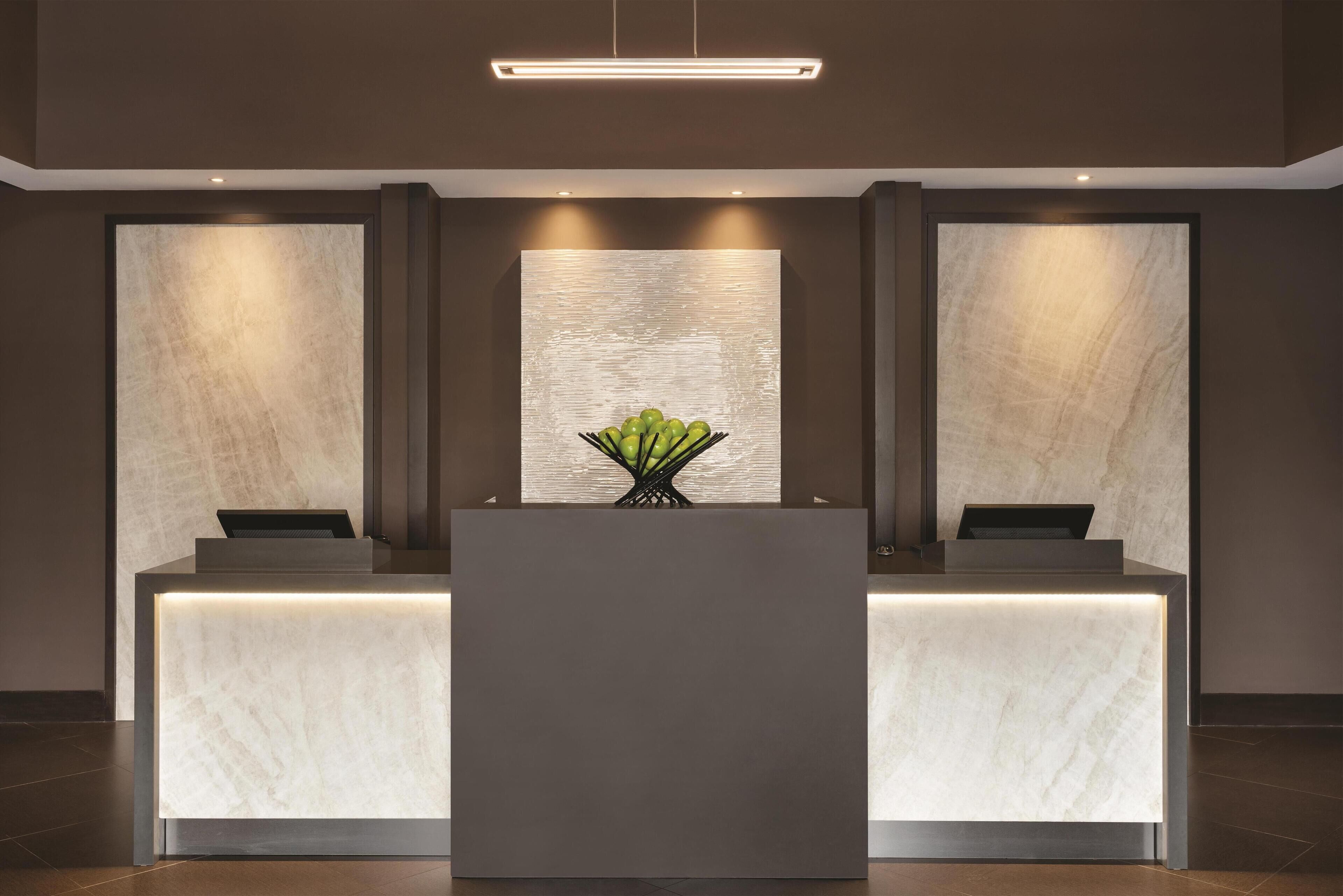 A reception desk with a modern design, featuring a marble-like surface and a central vase with green foliage.