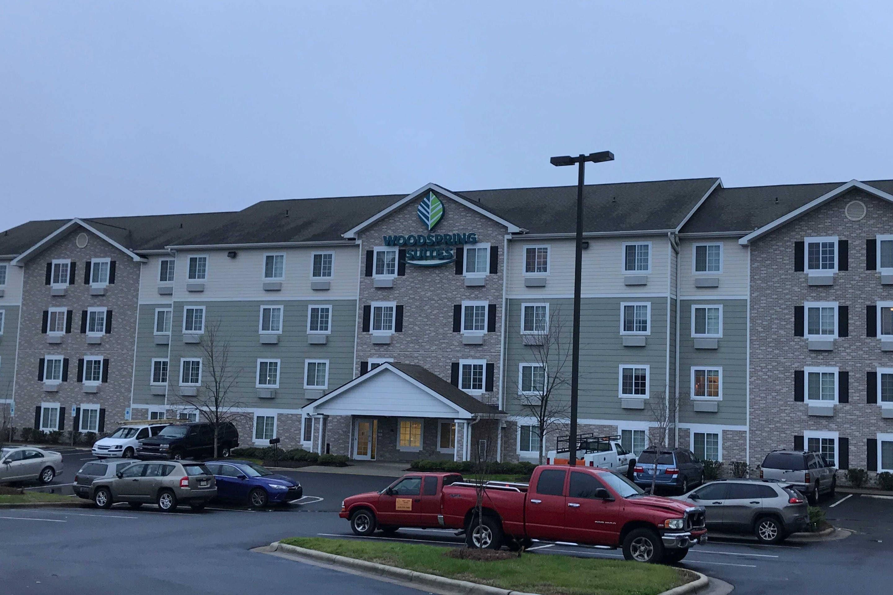 A multi-story hotel with a central entrance, parking lot, and several vehicles parked in front.