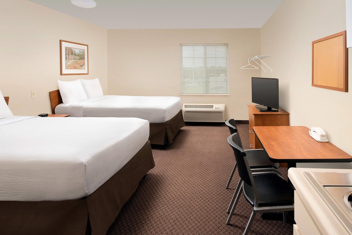 A hotel room with two beds, a desk with a computer, a chair, a TV, and a window with blinds.