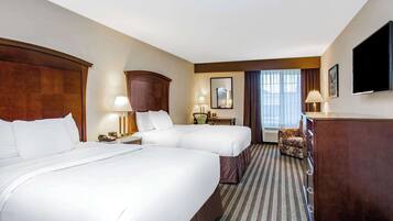 A hotel room with two beds, a desk, a chair, a TV, and a window with curtains.