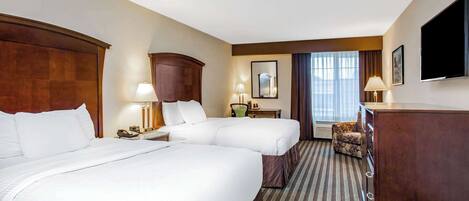 A hotel room with two beds, a desk, a chair, a TV, and a window with curtains.