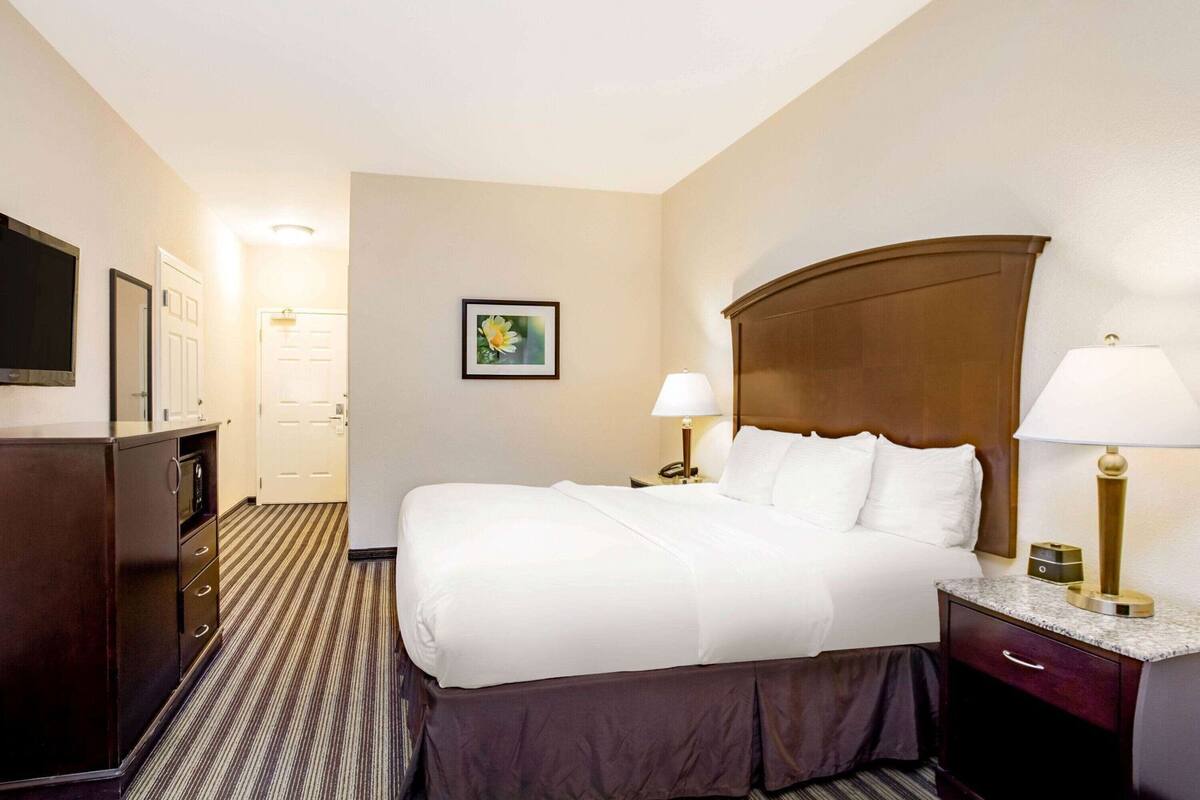 A hotel room with a bed, bedside tables, a TV, a desk, and a chair.