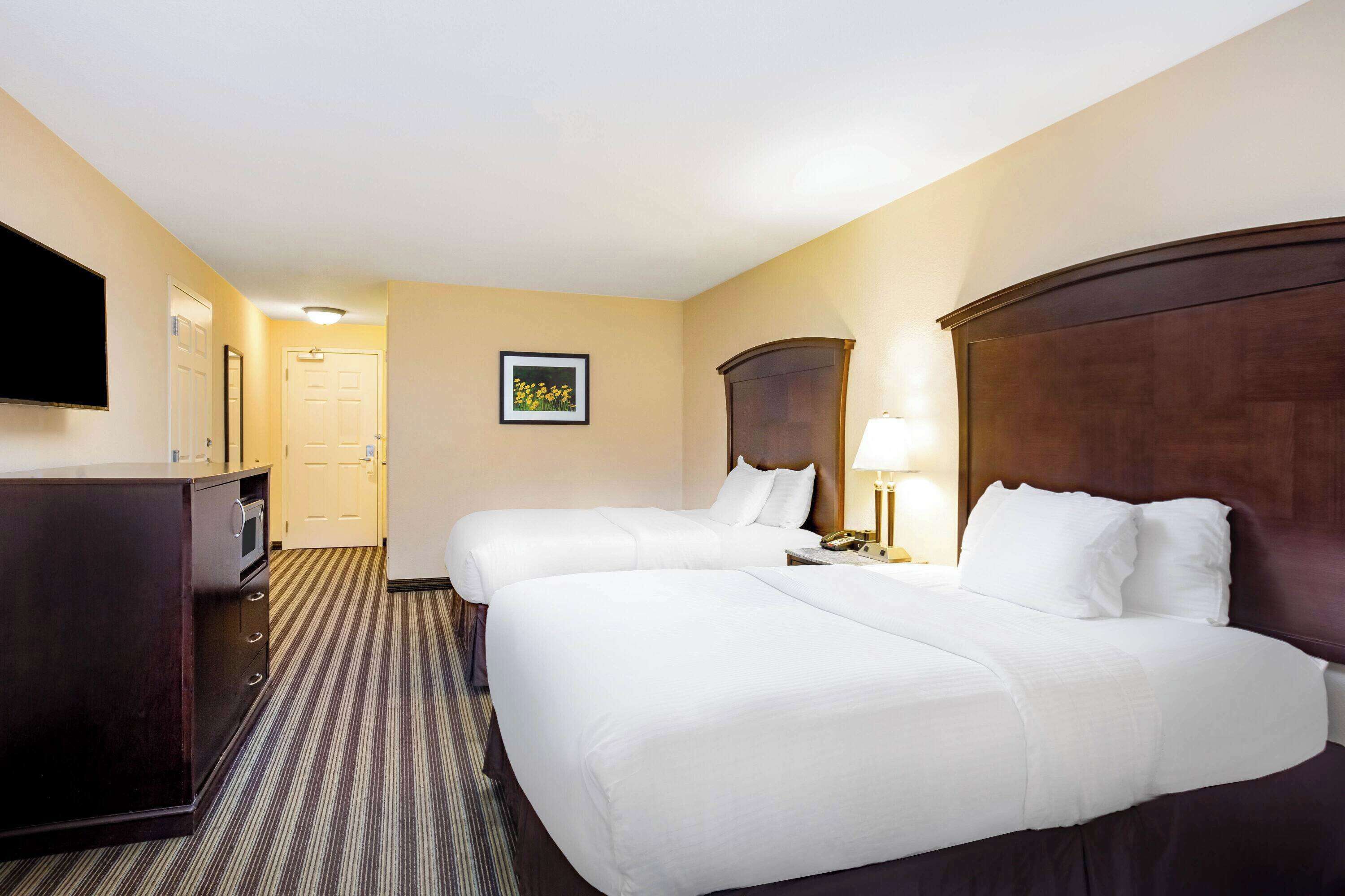 A hotel room with two beds, a desk, a television, and a framed picture on the wall.