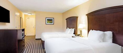 A hotel room with two beds, a desk, a television, and a framed picture on the wall.