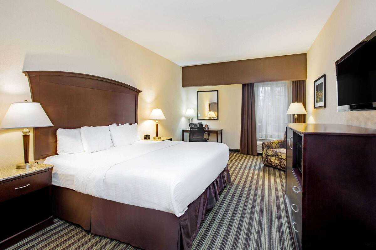 A hotel room with a large bed, two bedside lamps, a desk with a chair, a television, and a large mirror on the wall.