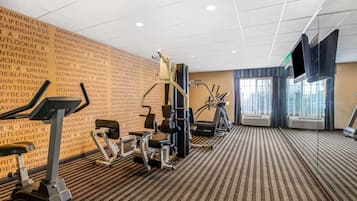 Un gimnasio con diversos equipos de ejercicio, una pared grande con texto motivacional y una pantalla de televisión.