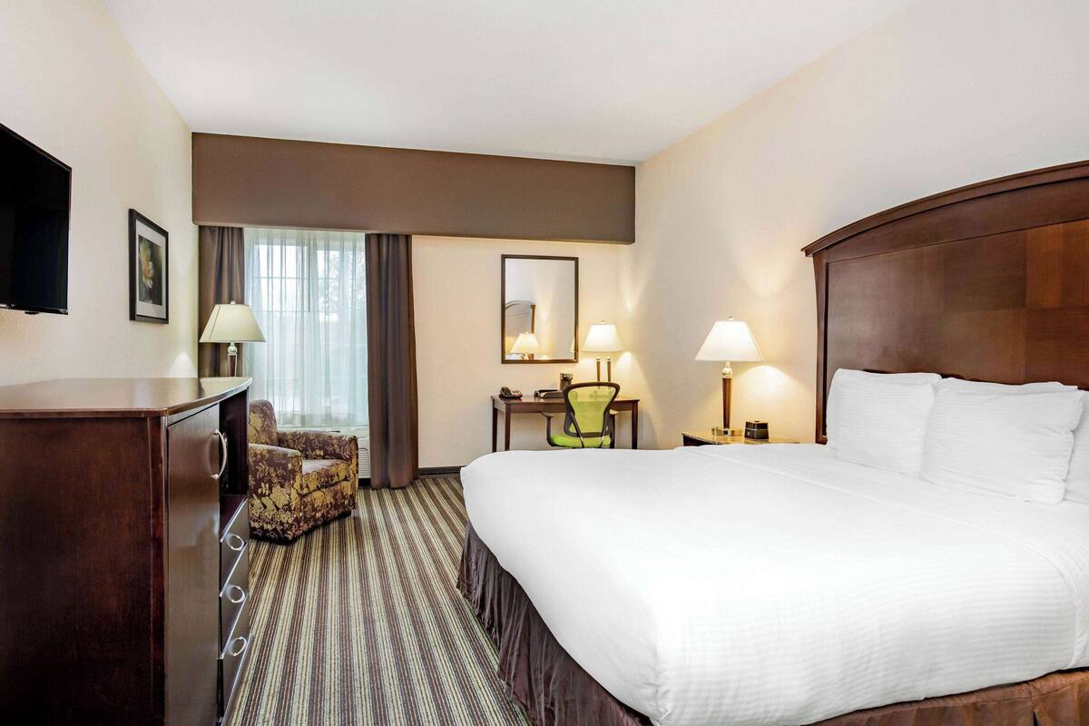 A hotel room with a large bed, a desk with a chair, a television, and a window with curtains.