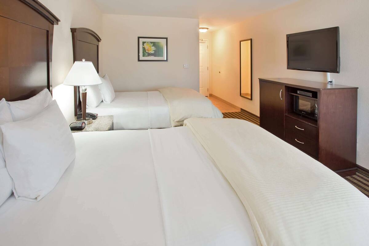 A hotel room with two beds, a TV, a desk with a lamp, and a small cabinet.