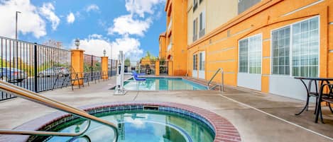 Un área de piscina con borde de ladrillo, una escalera metálica y una mesa con sillas.