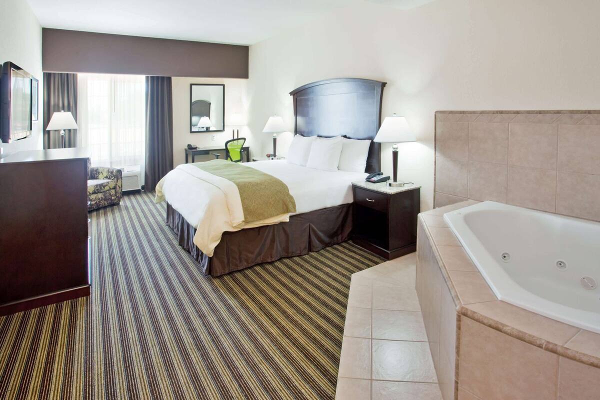 A hotel room with a large bed, a separate bathroom with a bathtub, a desk, and a chair.