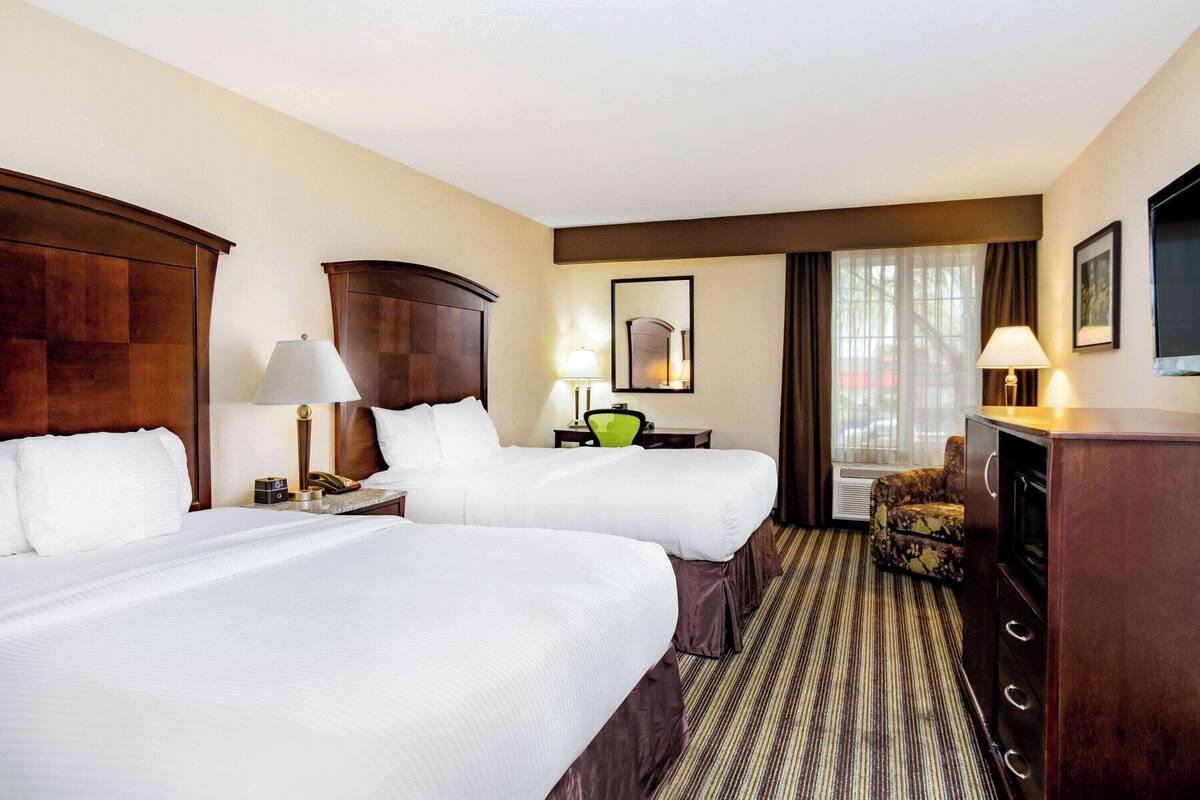 A hotel room with two beds, a desk, a chair, a TV, and a window with curtains.