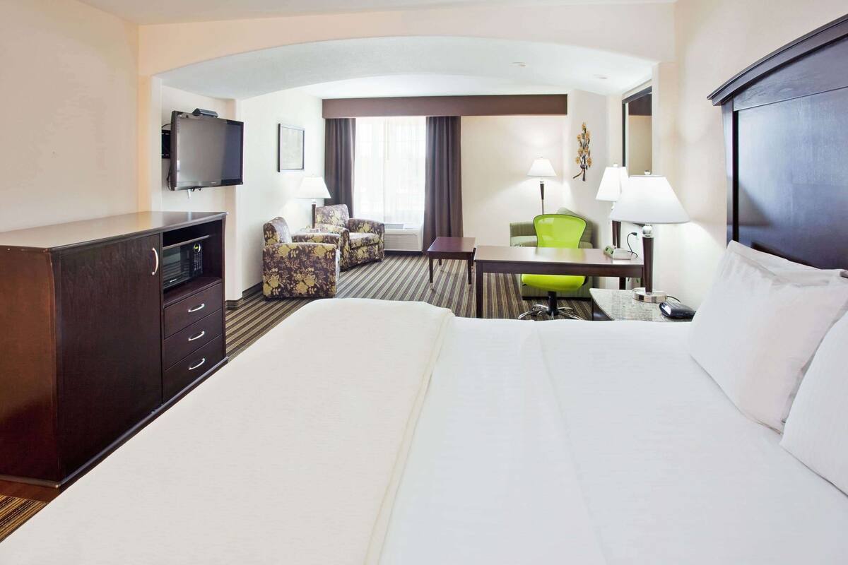 A hotel room with a large bed, a desk, a chair, a television, and a flat-screen TV mounted on the wall.