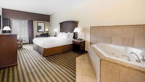 A hotel room with a large bed, a desk, a chair, a nightstand, a lamp, and a bathtub. - La Quinta Inn & Suites by Wyndham Fowler (Fowler)
