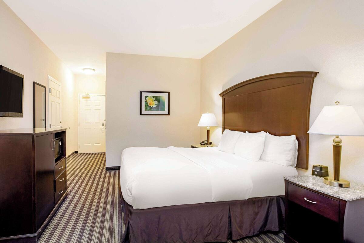 A hotel room with a bed, bedside lamps, a dresser, a TV, and a framed picture on the wall.