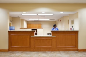 A reception area with a wooden reception desk, a flat-screen TV, and a sign indicating a priority club.