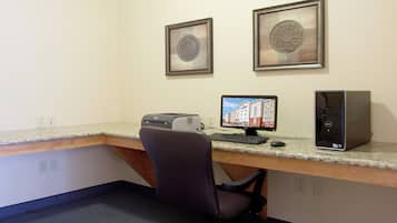 A workspace with a desktop computer, a printer, and a chair. There are two framed pictures on the wall.