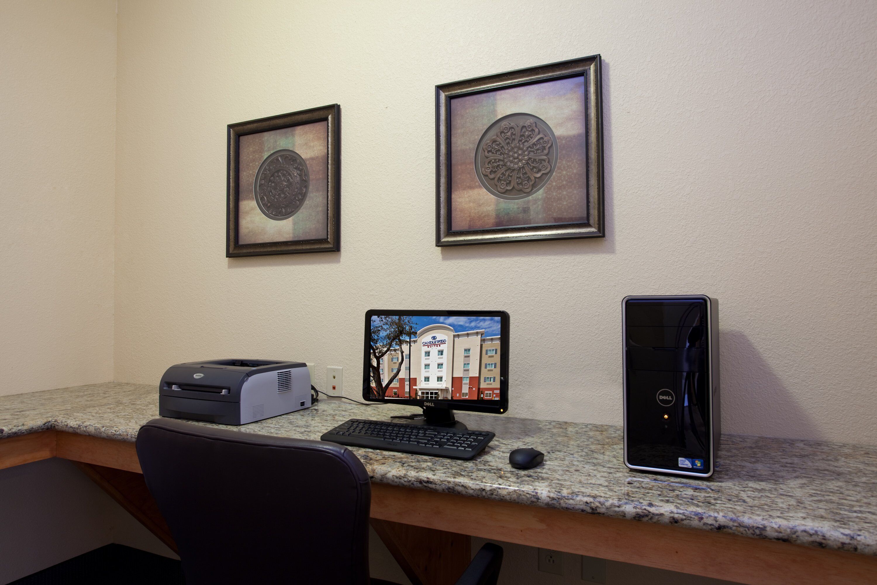 A desk with a desktop computer, a printer, and a monitor displaying a hotel building.