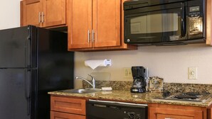A kitchen with wooden cabinets, a black refrigerator, a microwave, a dishwasher, and a granite countertop.