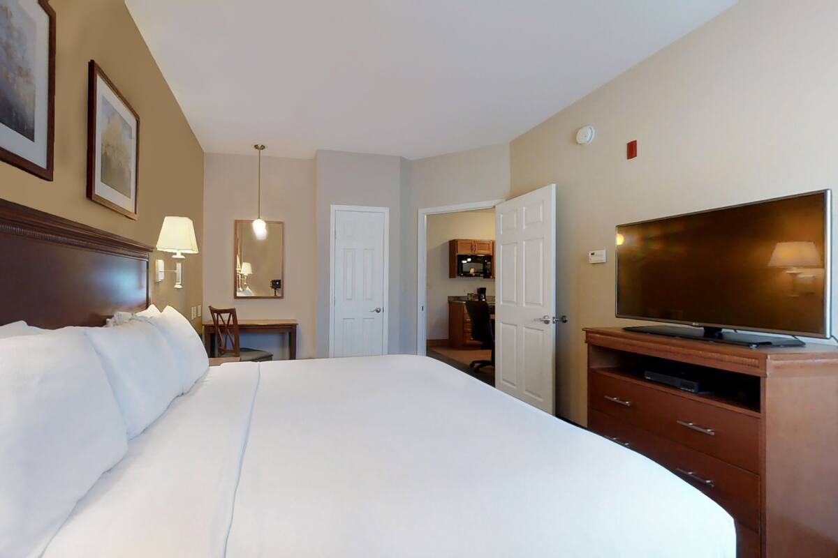 Une chambre d’hôtel avec un grand lit, une télévision, un bureau avec une chaise et une porte donnant sur une salle de bain.