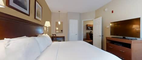 A hotel room with a large bed, a television, a desk with a chair, and a door leading to a bathroom.