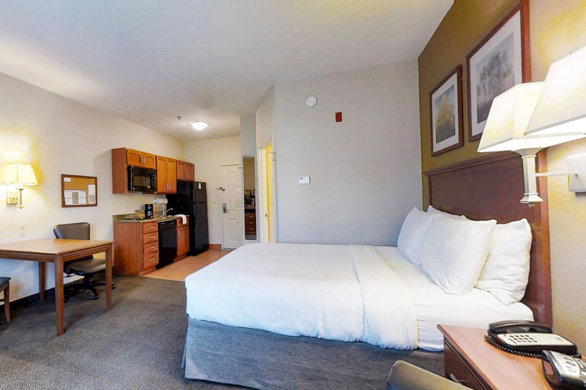 Une chambre d’hôtel équipée d’un lit, d’un bureau, d’une chaise, d’une kitchenette et d’un téléphone posé sur la table de chevet.